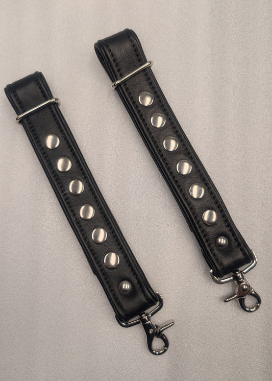Two black leather straps with silver studs and metal clasps on a light gray background