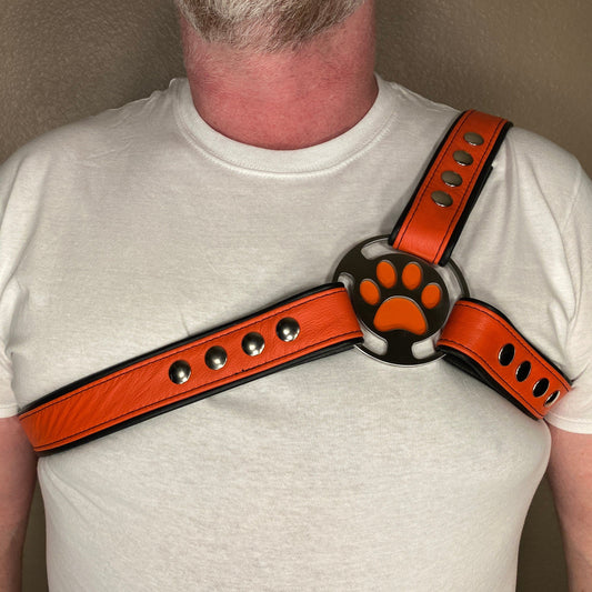 A person wearing a white t-shirt modeling a puppy-themed three strap harness in orange and black with a paw print design.